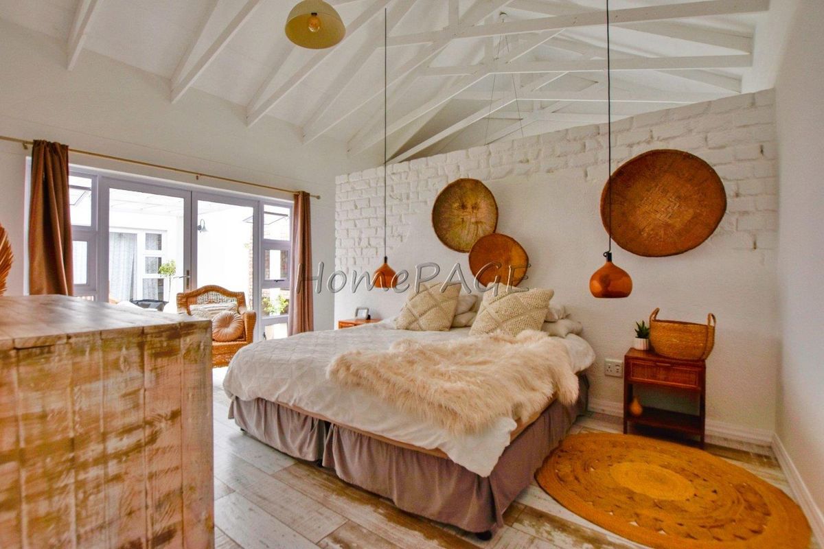Spacious bedroom featuring a vaulted exposed beam ceiling, white painted brick feature wall, and large glass sliding doors leading to an outdoor area.