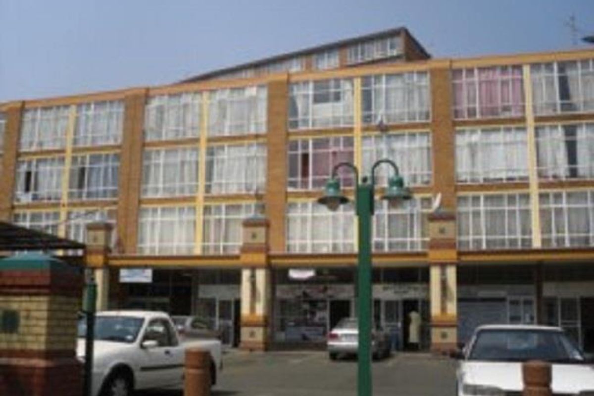 Front elevation of a multi-story commercial building featuring large glass window panels and a paved parking area.