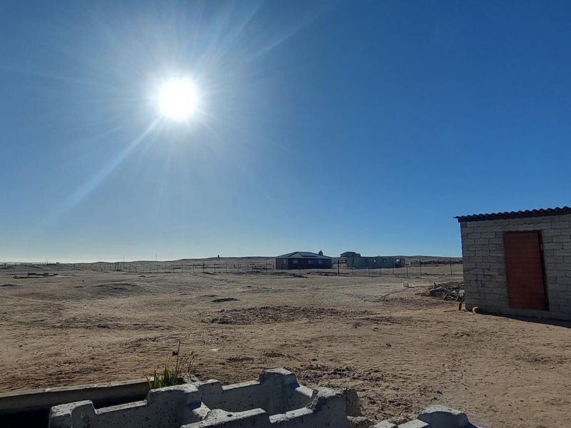 Wide-angle view of the expansive small holding grounds featuring basic outbuildings, perimeter fencing, and undeveloped sandy terrain under a clear sky.