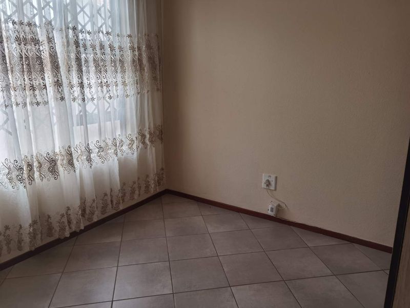An empty bedroom featuring neutral wall paint, tiled flooring, and a window fitted with a security gate and curtains.