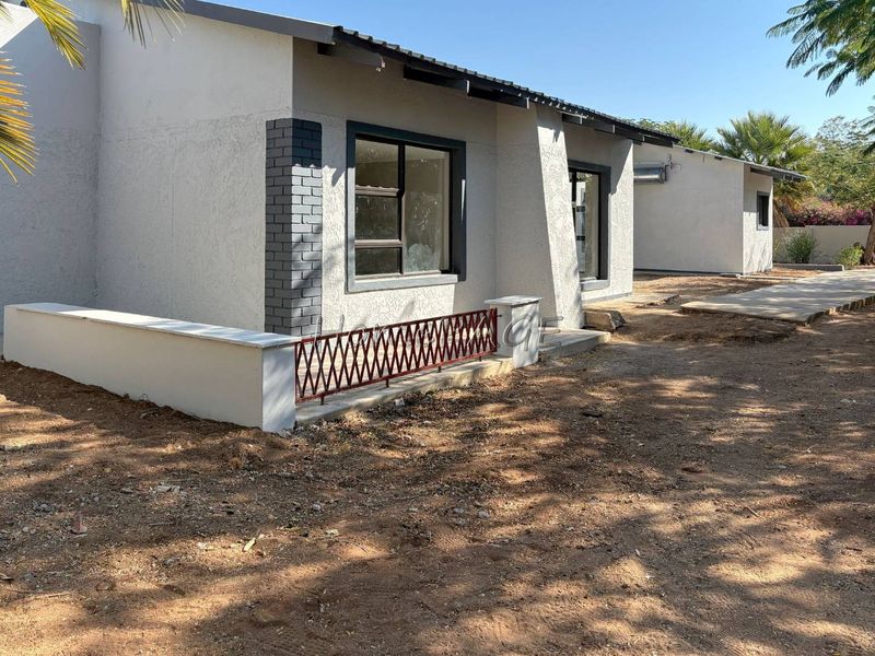 Rear exterior view of the house featuring a concrete patio, low masonry wall with metal railing, and aluminium window frames.