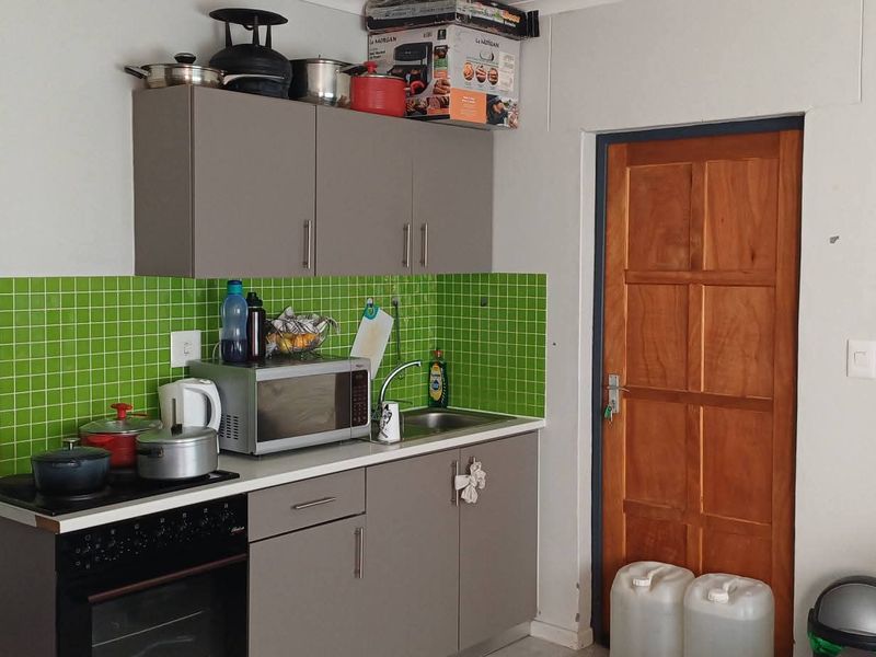 Compact kitchen area featuring grey cabinetry, a vibrant green mosaic tile backsplash, built-in oven, and hob, adjacent to a traditional wooden door.