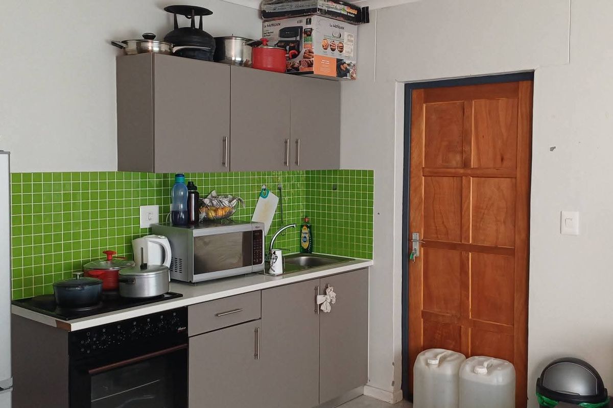 Compact kitchen area featuring grey cabinetry, a vibrant green mosaic tile backsplash, built-in oven, and hob, adjacent to a traditional wooden door.