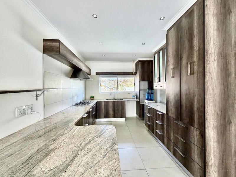 Modern kitchen featuring extensive wood-grain cabinetry, granite countertops, a gas hob with extractor fan, and tiled flooring in a clean, well-lit space.