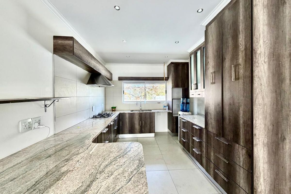 Modern kitchen featuring extensive wood-grain cabinetry, granite countertops, a gas hob with extractor fan, and tiled flooring in a clean, well-lit space.