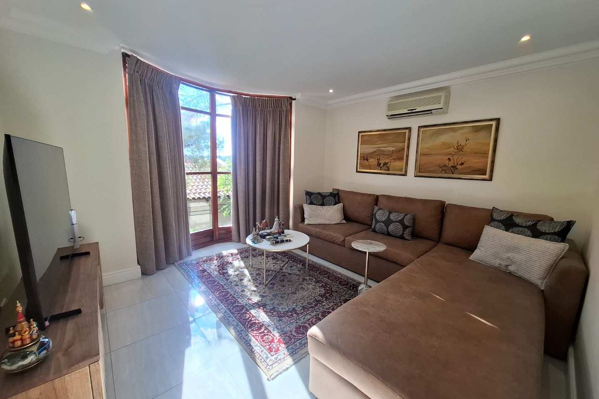 A comfortable living room featuring tiled flooring, recessed downlighting, a wall-mounted air conditioning unit, and a curved window with access to an outdoor area.