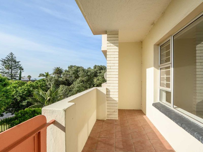 A covered balcony featuring tiled flooring, a brick support pillar, and metal railings, offering an open outdoor space with views of surrounding greenery.