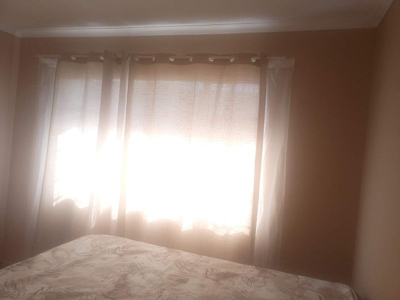 A bedroom interior featuring a window with installed curtain rods and ceiling coving, currently illuminated by bright natural light.