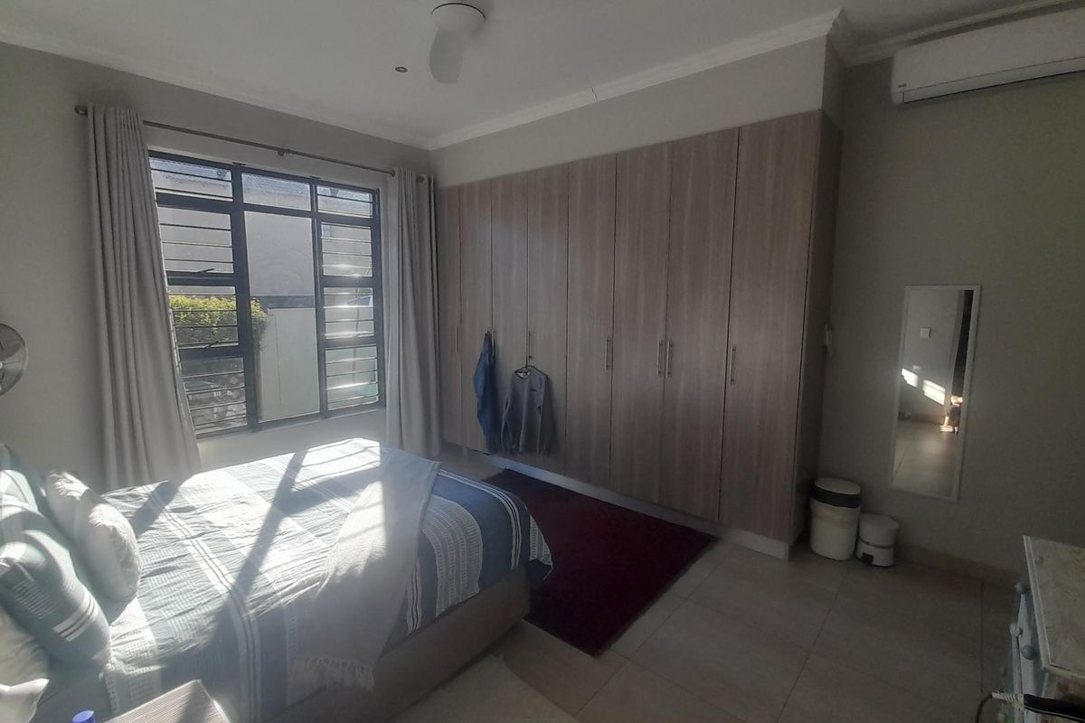 A well-lit bedroom featuring built-in wooden cabinetry, tiled flooring, and a wall-mounted air conditioning unit.