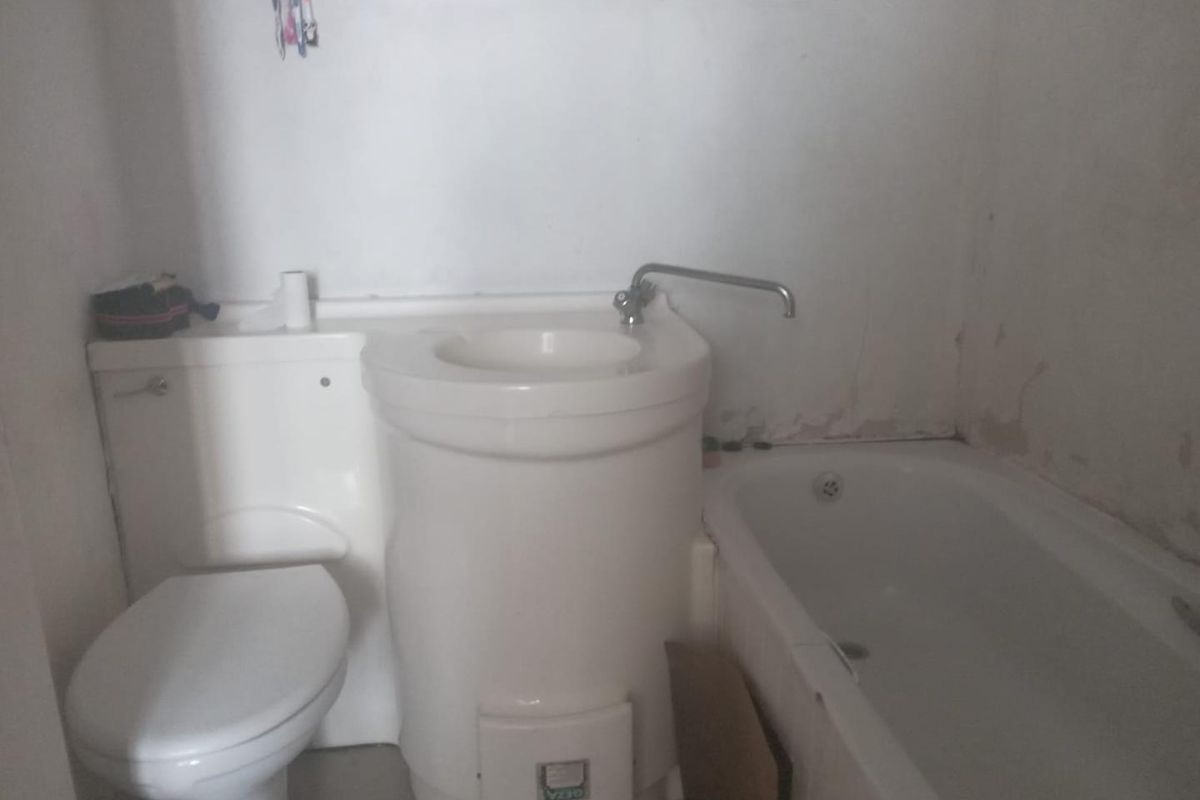 Compact bathroom featuring a combined toilet and basin unit alongside a standard bathtub, requiring cosmetic updates and wall repairs.