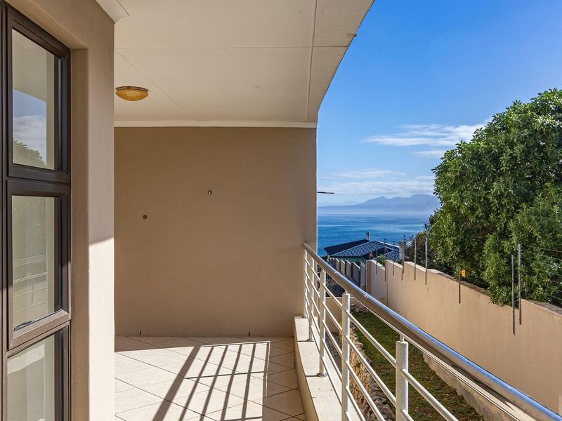 A spacious covered balcony featuring tiled flooring, a stainless steel balustrade, and expansive ocean and mountain views.