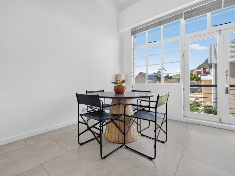Bright living area featuring large windows and a glass door leading to a balcony, finished with neutral floor tiles and clean white walls.