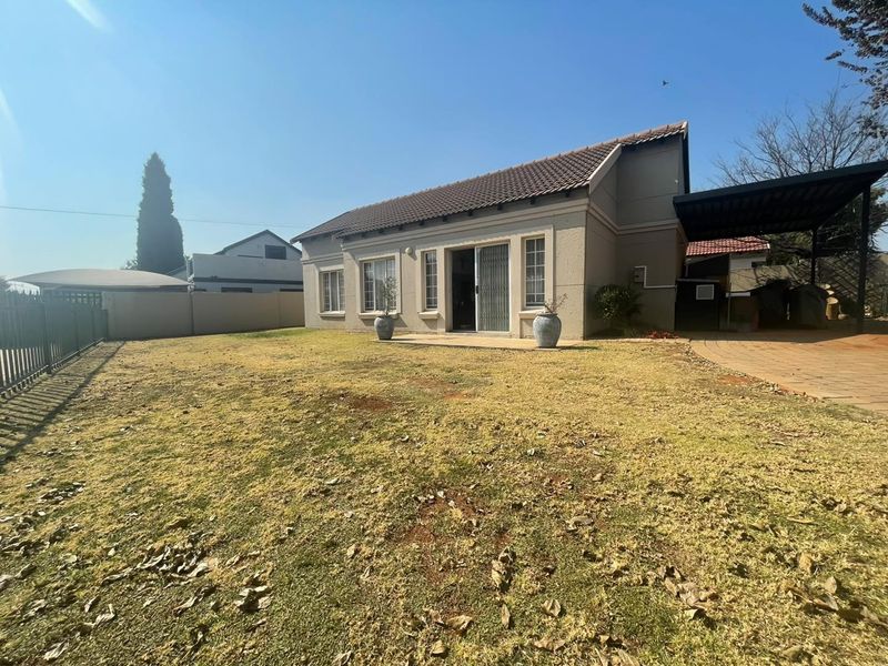 Rear view of the property featuring a tiled roof, sliding glass door access, a paved driveway with carport, and a private garden area.