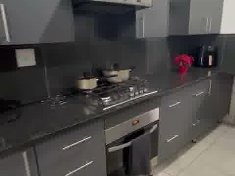 Modern kitchen featuring dark grey cabinetry, stone countertops, integrated gas hob, built-in oven, and extractor fan with light-colored tiled flooring.
