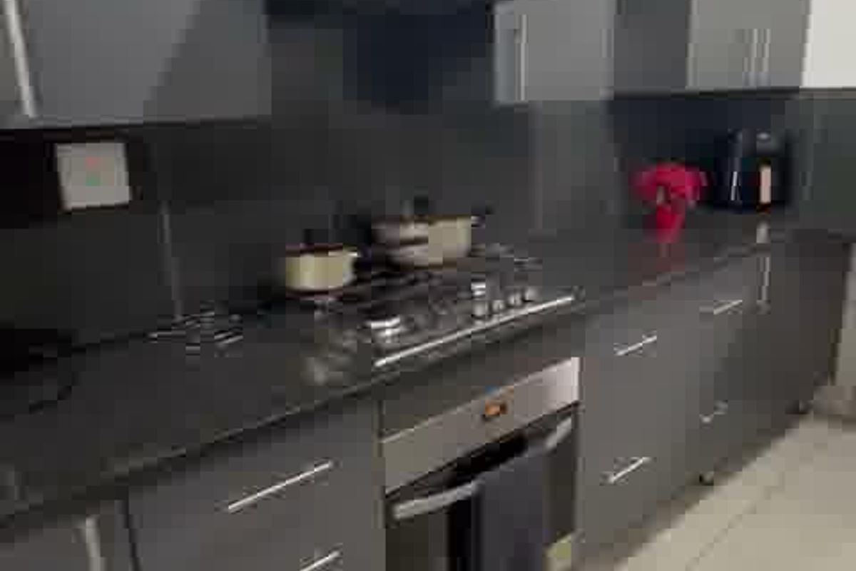 Modern kitchen featuring dark grey cabinetry, stone countertops, integrated gas hob, built-in oven, and extractor fan with light-colored tiled flooring.