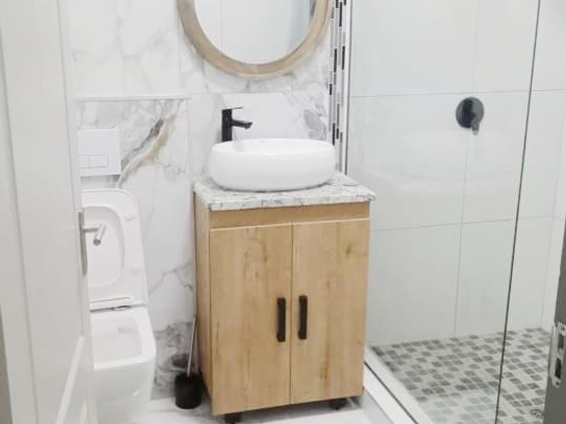 Modern bathroom featuring a walk-in shower with glass screen, wall-mounted toilet, and a vanity unit with a vessel sink and marble-effect tiling.