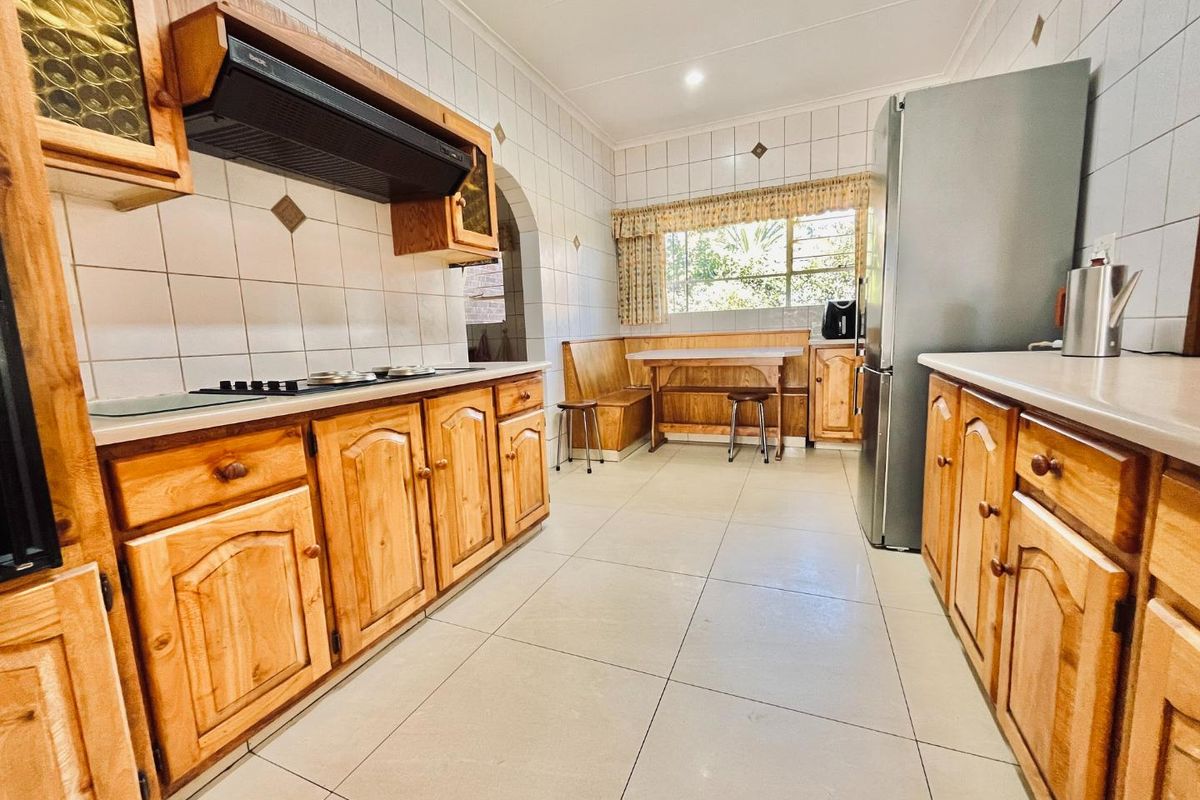 A functional kitchen featuring wooden cabinetry, tiled walls, a built-in hob with extractor fan, and a dedicated breakfast nook area.