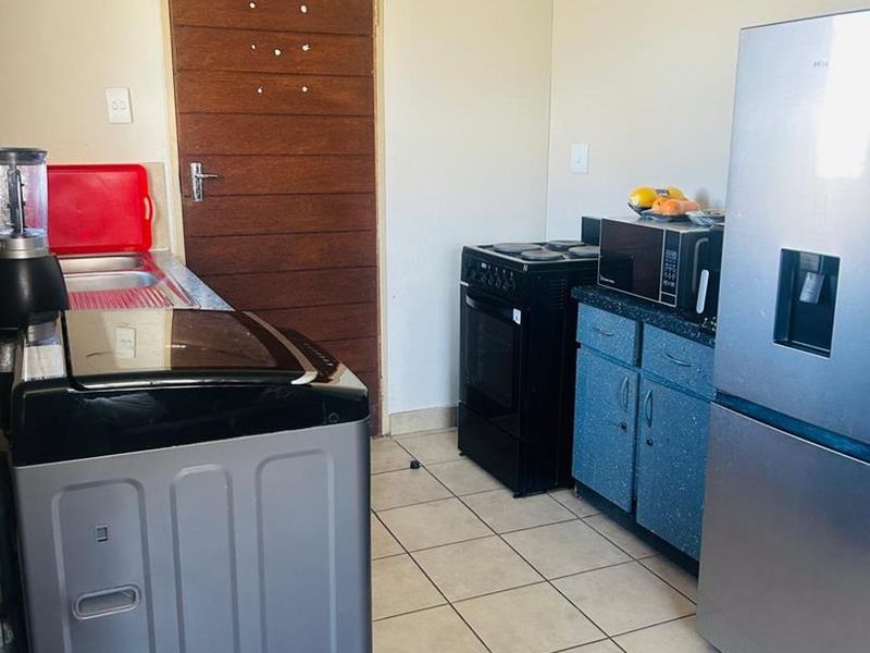 A functional kitchen area featuring tiled flooring, built-in cabinetry with laminate countertops, a stainless steel sink, and a freestanding stove.