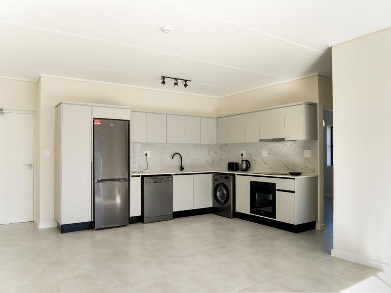 Modern open-plan kitchen featuring sleek cabinetry, stone-look backsplash, integrated oven, extractor fan, and neutral tiled flooring in a clean, contemporary apartment setting.