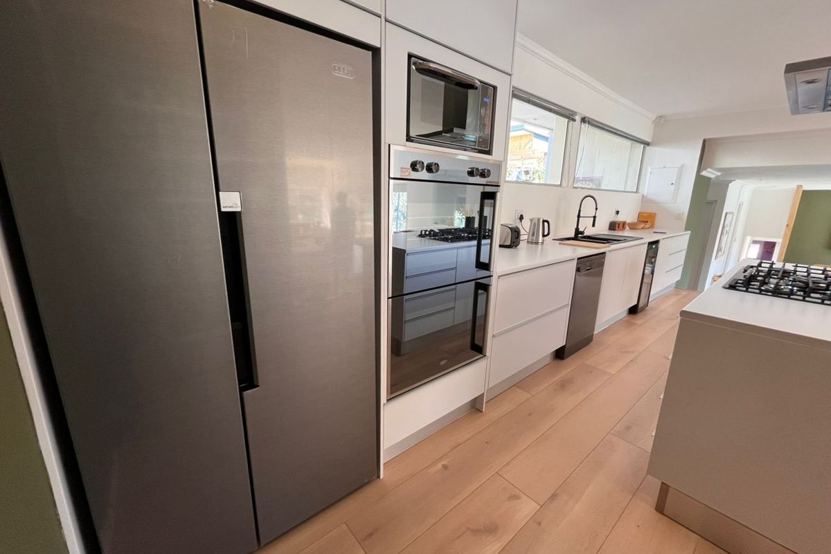 Modern kitchen featuring sleek white cabinetry, integrated stainless steel appliances, a gas hob, and light wood-look flooring.
