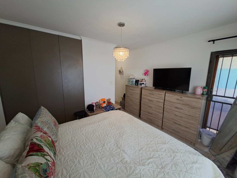 A bedroom featuring built-in cupboards, a decorative crystal pendant light, and direct access to an outdoor area through a security gate.