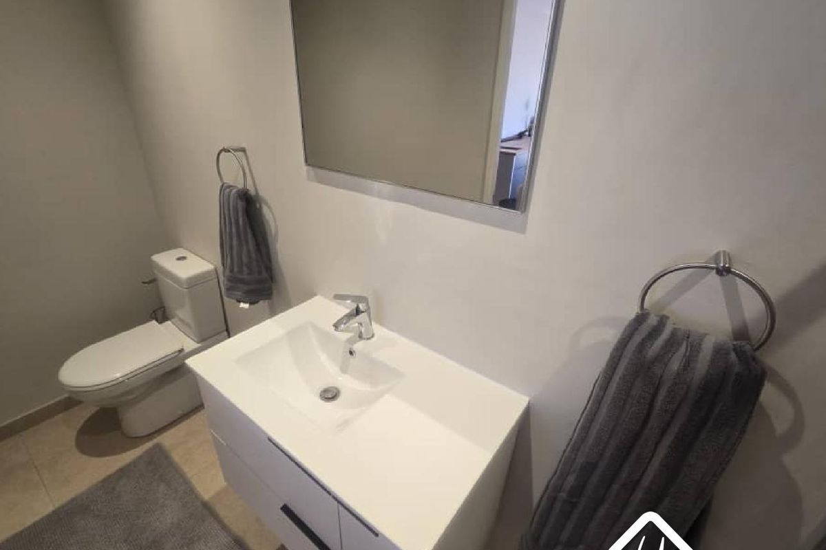 A modern bathroom featuring a sleek vanity with a basin, a wall-mounted mirror, and a contemporary toilet.