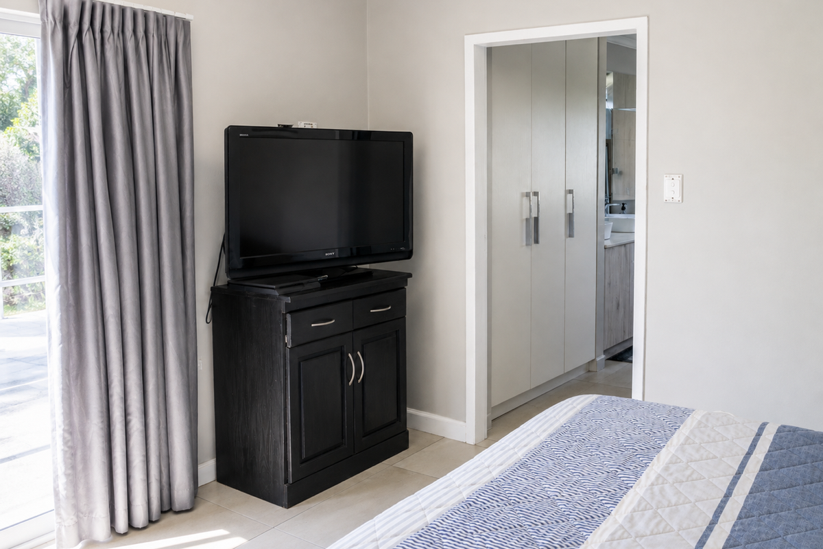 A well-lit bedroom featuring neutral walls, tiled flooring, built-in cupboards, and a sliding glass door providing access to the outdoor area.