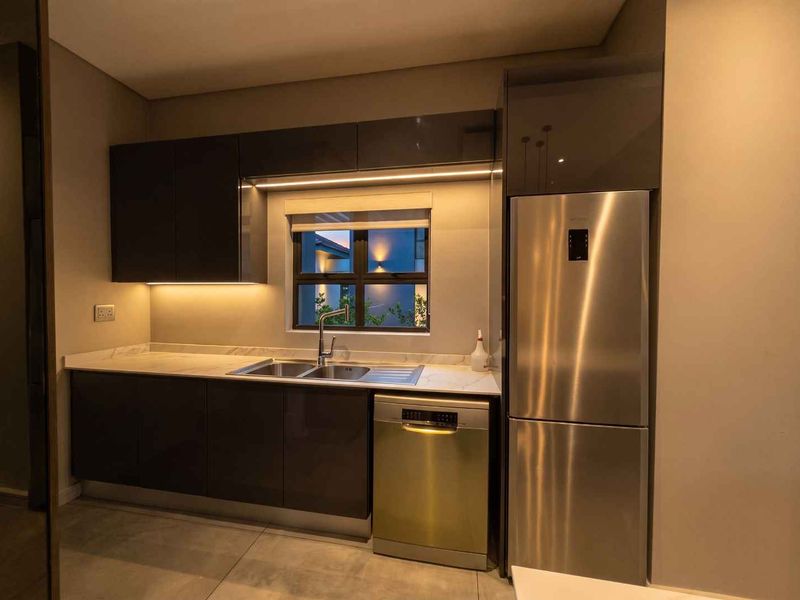 Modern kitchen featuring sleek dark glossy cabinetry, stone countertops, integrated dishwasher, and ambient under-cabinet lighting.