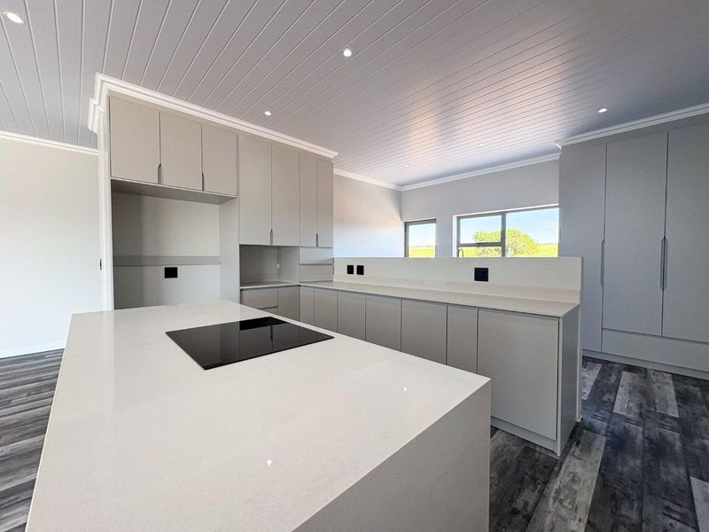 Modern, minimalist kitchen featuring sleek grey cabinetry, stone countertops, a central island with an integrated hob, and stylish tongue and groove ceiling detailing.