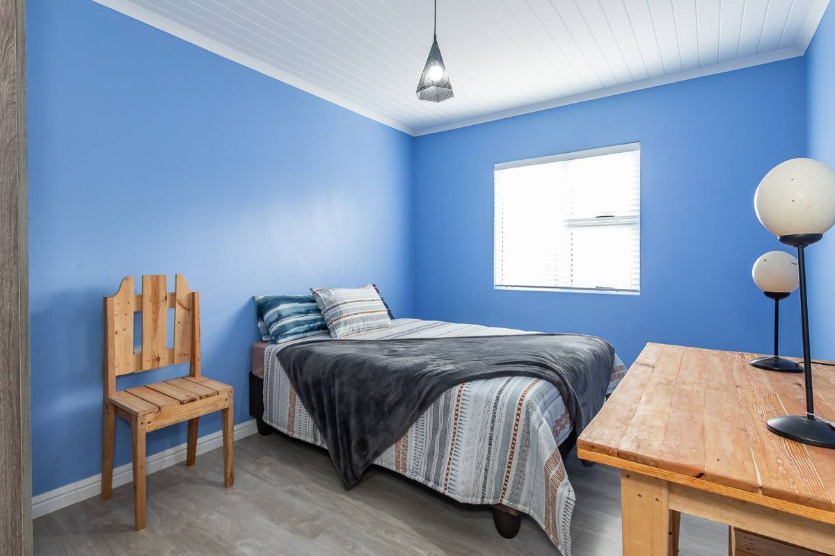 A bedroom featuring blue painted walls, wood-look laminate flooring, and a white tongue-and-groove ceiling.