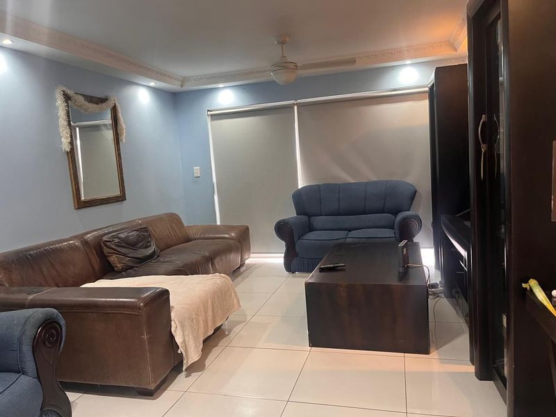 A living room featuring tiled flooring, crown molding, recessed lighting, and a ceiling fan, with roller blinds covering the windows.