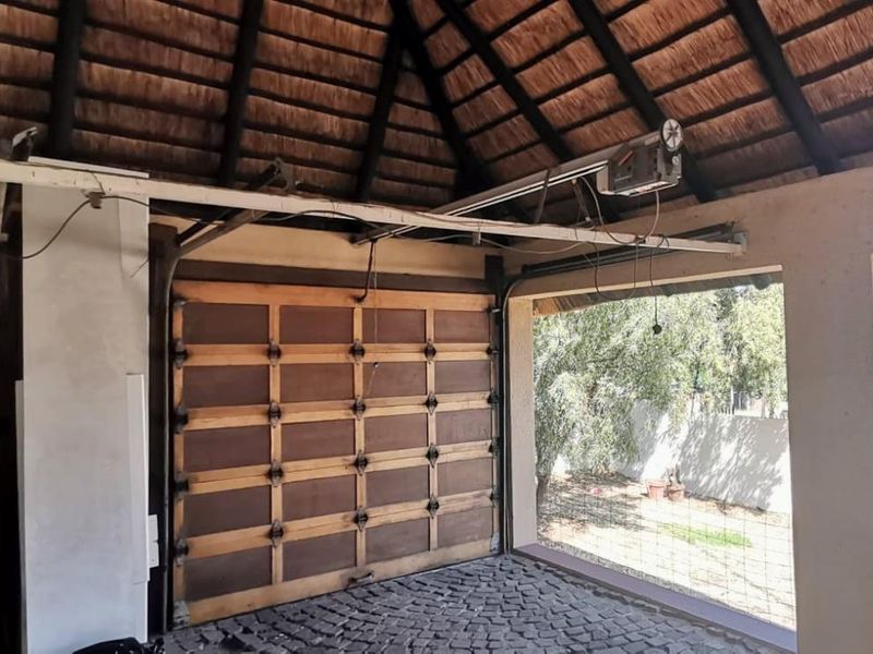A rustic garage featuring a traditional thatched roof with exposed timber rafters, a sectional wooden garage door, and durable cobblestone flooring.