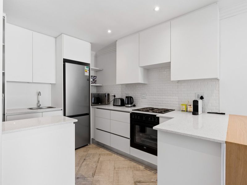 Modern kitchen featuring white cabinetry, stone countertops, subway tile backsplash, built-in oven, gas hob, and stylish herringbone flooring.