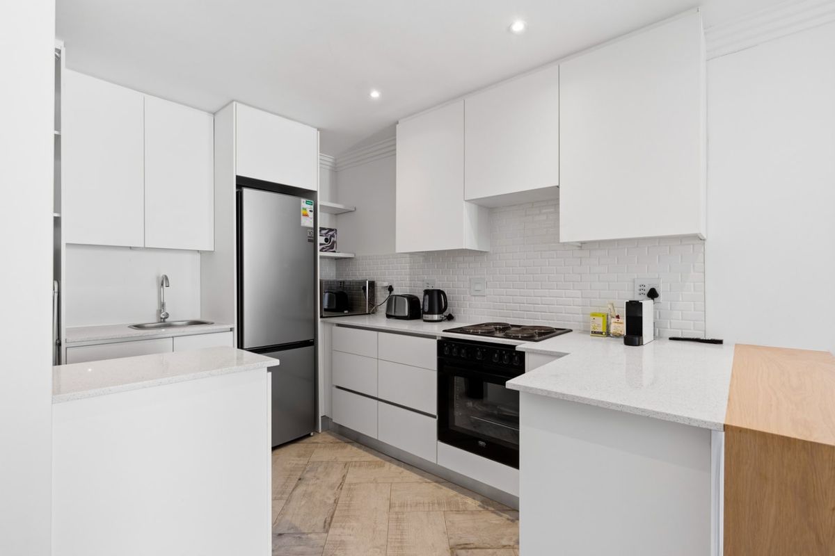Modern kitchen featuring white cabinetry, stone countertops, subway tile backsplash, built-in oven, gas hob, and stylish herringbone flooring.