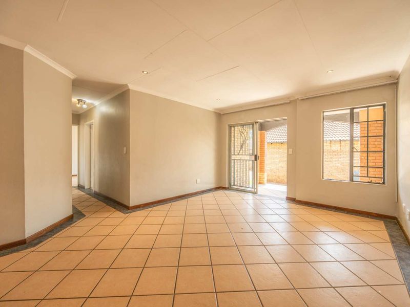 A spacious, empty living area featuring neutral walls, tiled flooring, and direct access to an outdoor patio through a security gate.