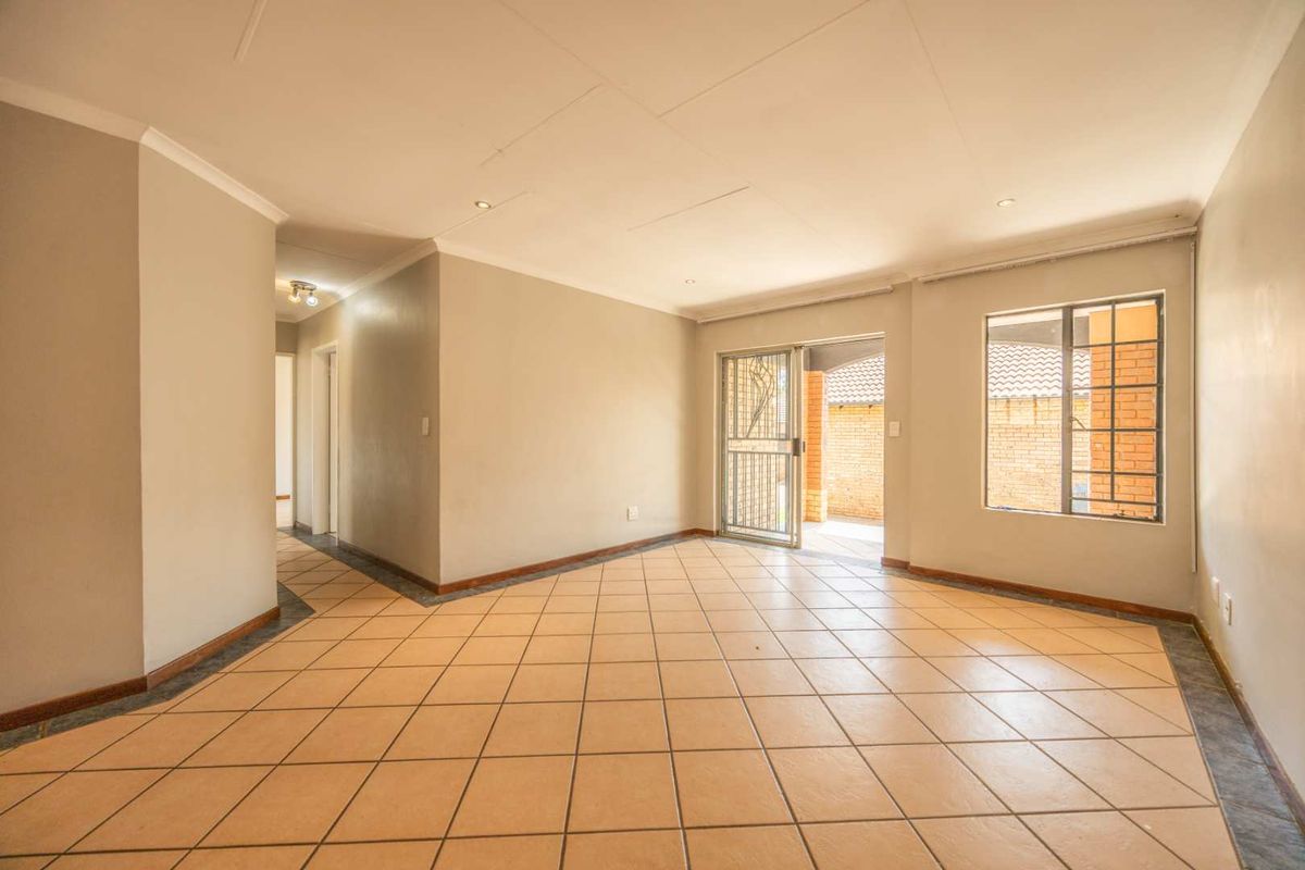 A spacious, empty living area featuring neutral walls, tiled flooring, and direct access to an outdoor patio through a security gate.