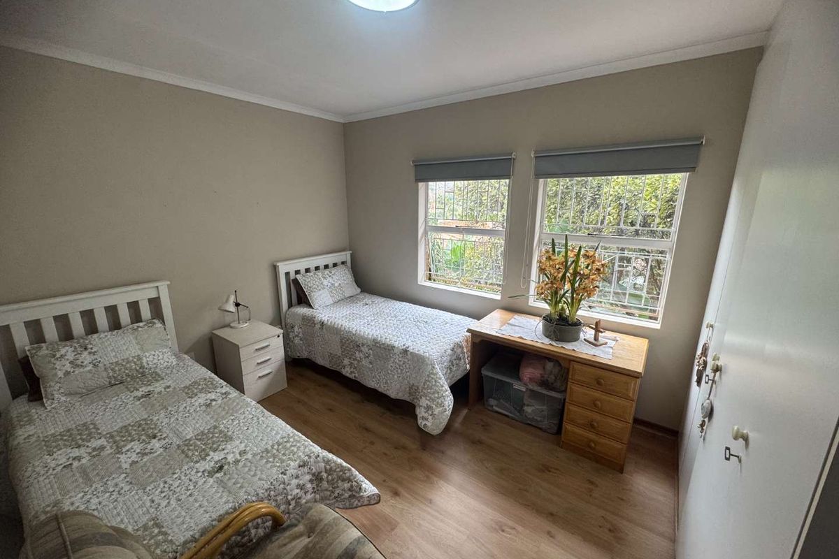 A functional bedroom featuring laminate flooring, built-in cupboards, and security bars on the windows.