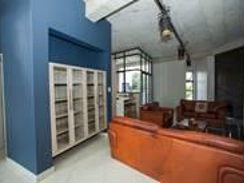 Spacious living area featuring modern track lighting, exposed concrete ceilings, tiled flooring, and a large built-in display cabinet.