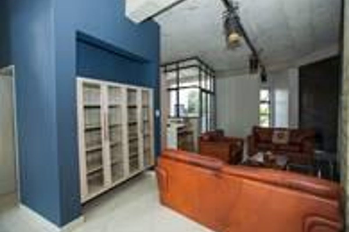 Spacious living area featuring modern track lighting, exposed concrete ceilings, tiled flooring, and a large built-in display cabinet.