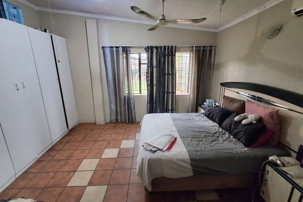 Spacious bedroom featuring built-in cupboards, tiled flooring, and a ceiling fan, with security bars on the windows.