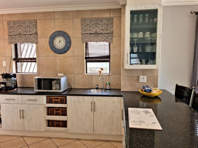 A functional kitchen featuring granite countertops, tiled backsplash, and ample built-in cabinetry with a glass-front display unit.