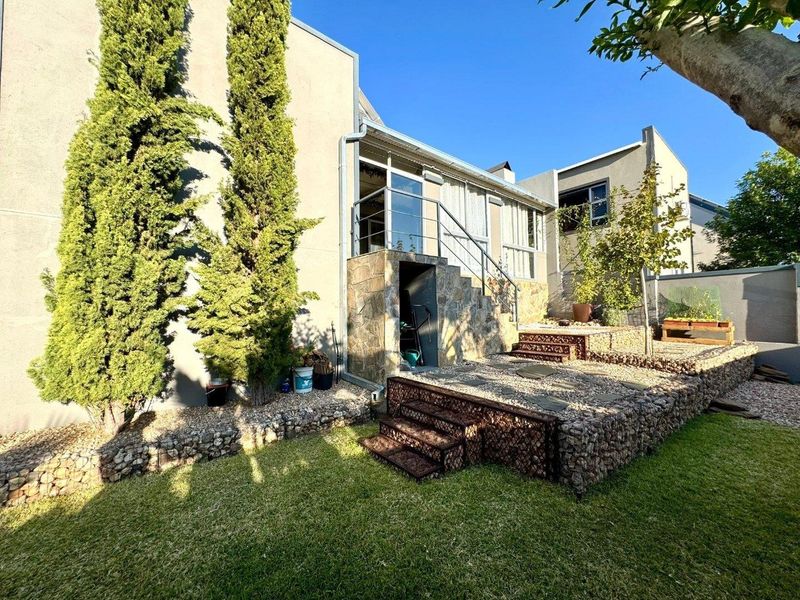 Rear exterior view featuring a raised gravel terrace with stone-clad retaining walls, metal staircase, and access to the upper level via glass sliding doors.