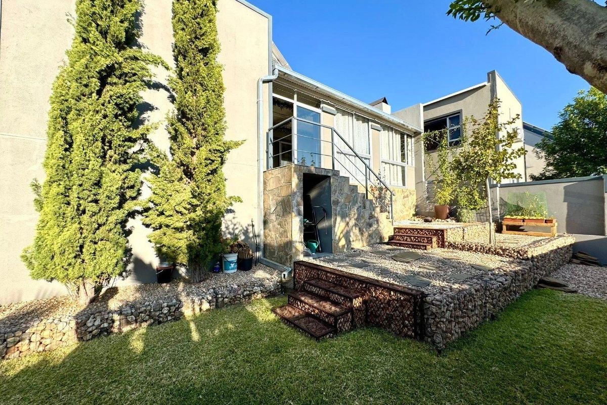 Rear exterior view featuring a raised gravel terrace with stone-clad retaining walls, metal staircase, and access to the upper level via glass sliding doors.