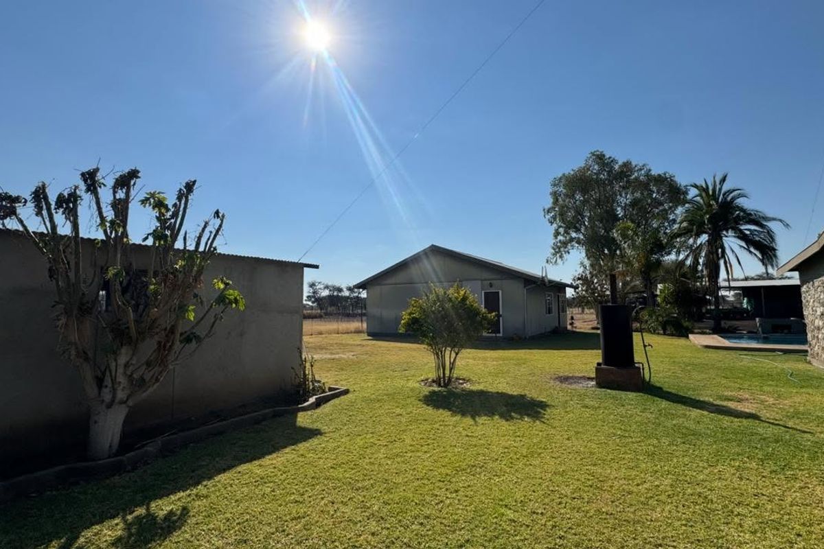 Spacious rear garden area featuring a well-maintained lawn, stone-clad exterior wall, and a water tank, set against a clear blue sky.