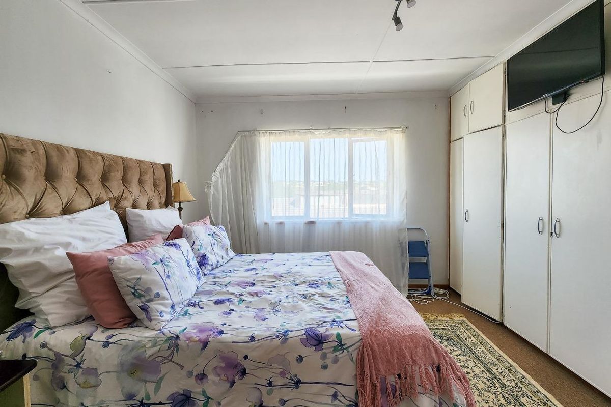 A functional bedroom featuring built-in wardrobes, neutral wall finishes, and a large window providing natural light.
