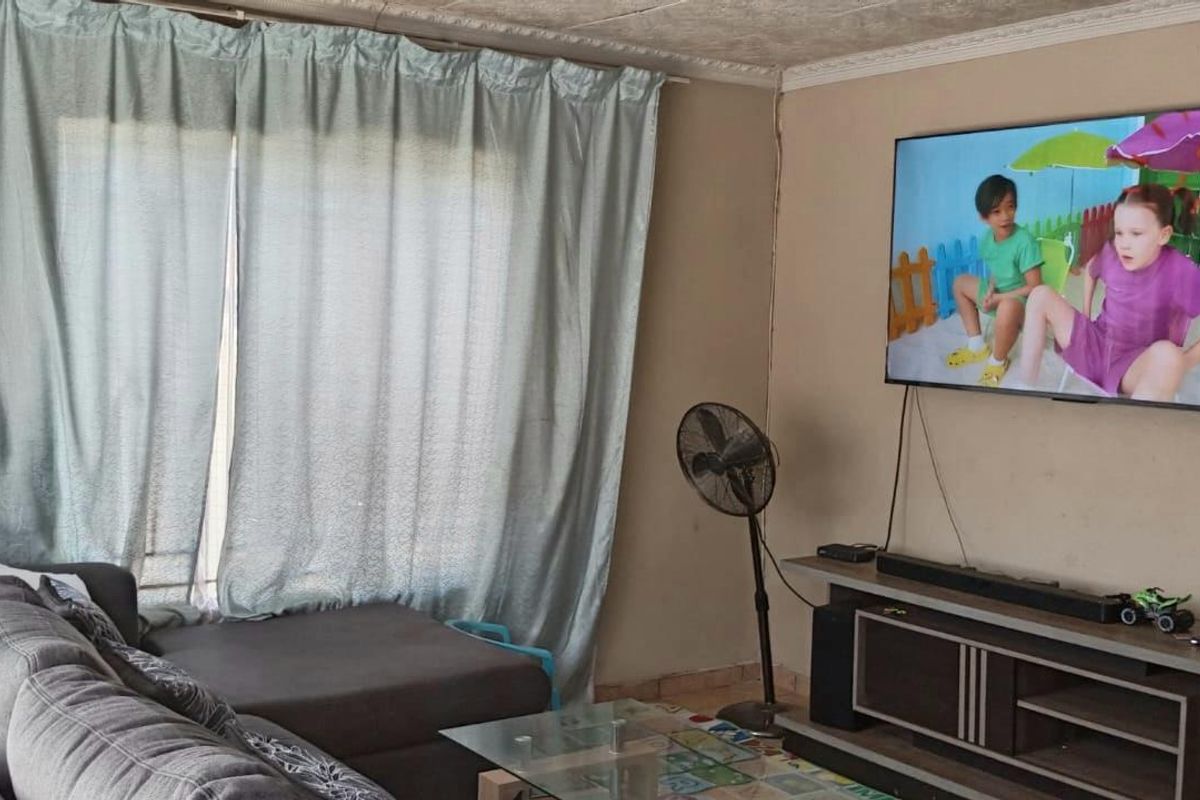 A living room featuring a wall-mounted television, large window with curtains, and tiled flooring.