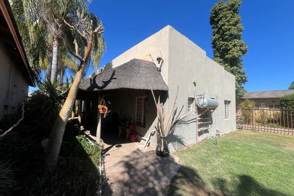 Rear view of the property featuring a thatched roof section, paved walkway, and an externally mounted solar geyser system.