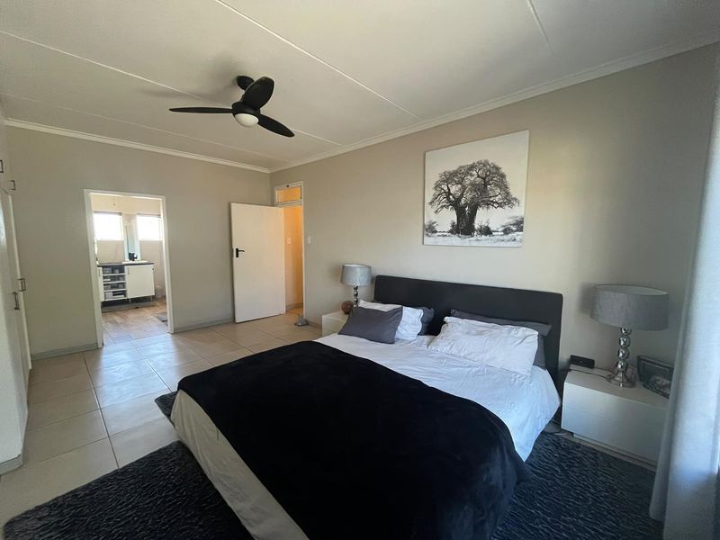 Spacious bedroom featuring neutral tiled flooring, a ceiling fan, and direct access to an en-suite bathroom with built-in storage.