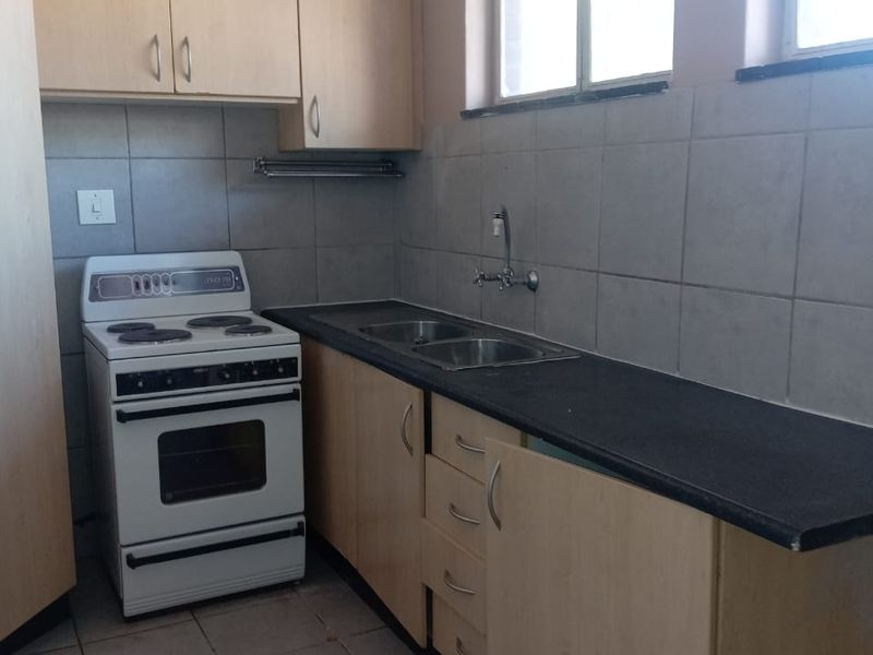A functional kitchen featuring light wood cabinetry, dark laminate countertops, a double sink, and a freestanding stove with tiled backsplash and flooring.
