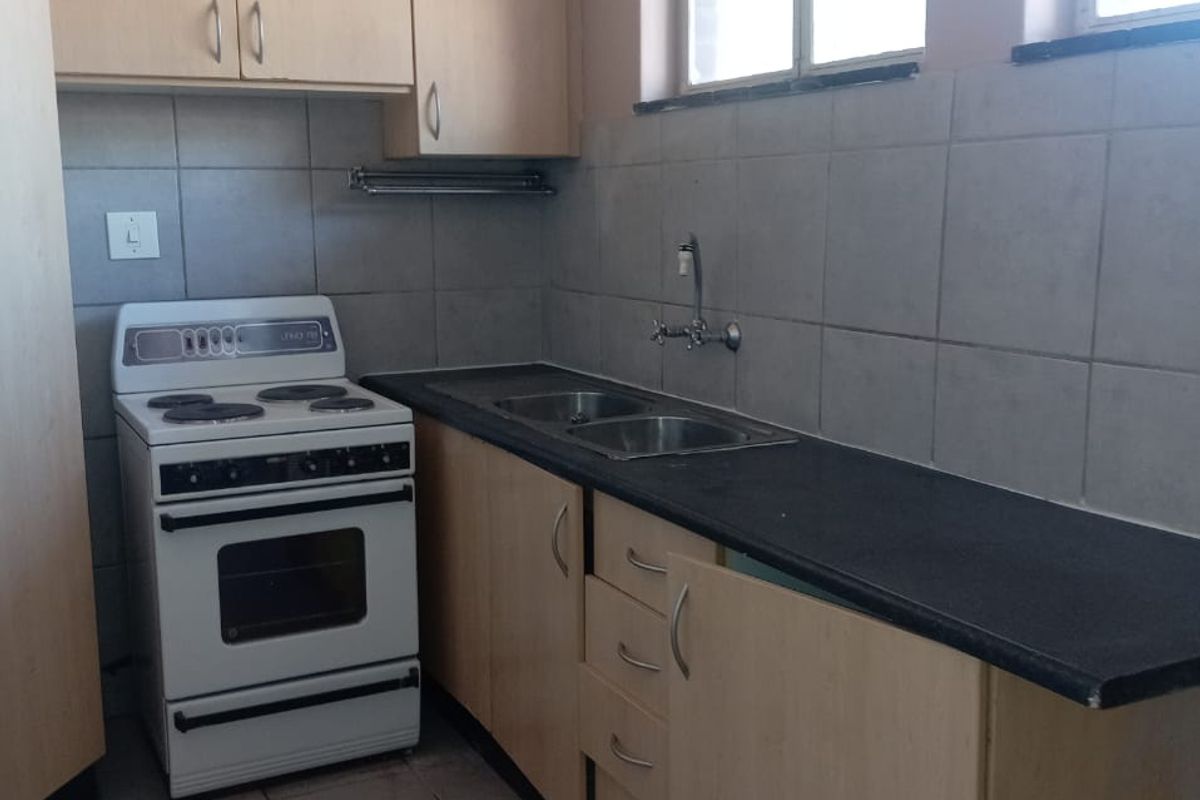 A functional kitchen featuring light wood cabinetry, dark laminate countertops, a double sink, and a freestanding stove with tiled backsplash and flooring.